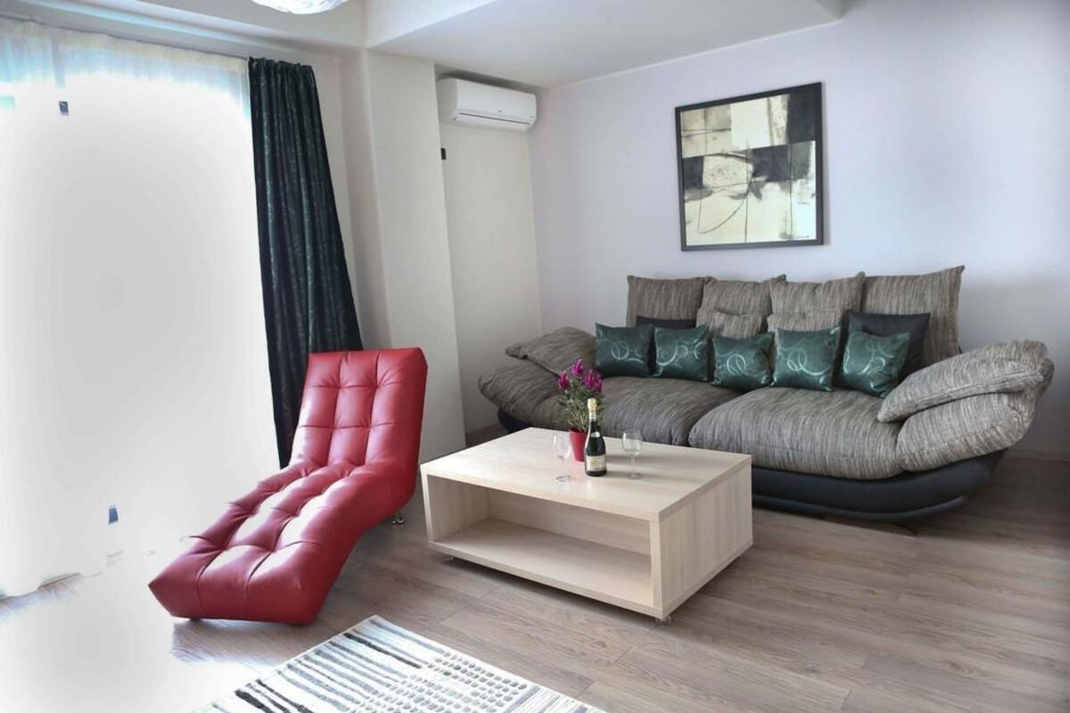 A modern living room with a red chair, a sofa with patterned cushions, a wooden coffee table, and a painting on the wall.
