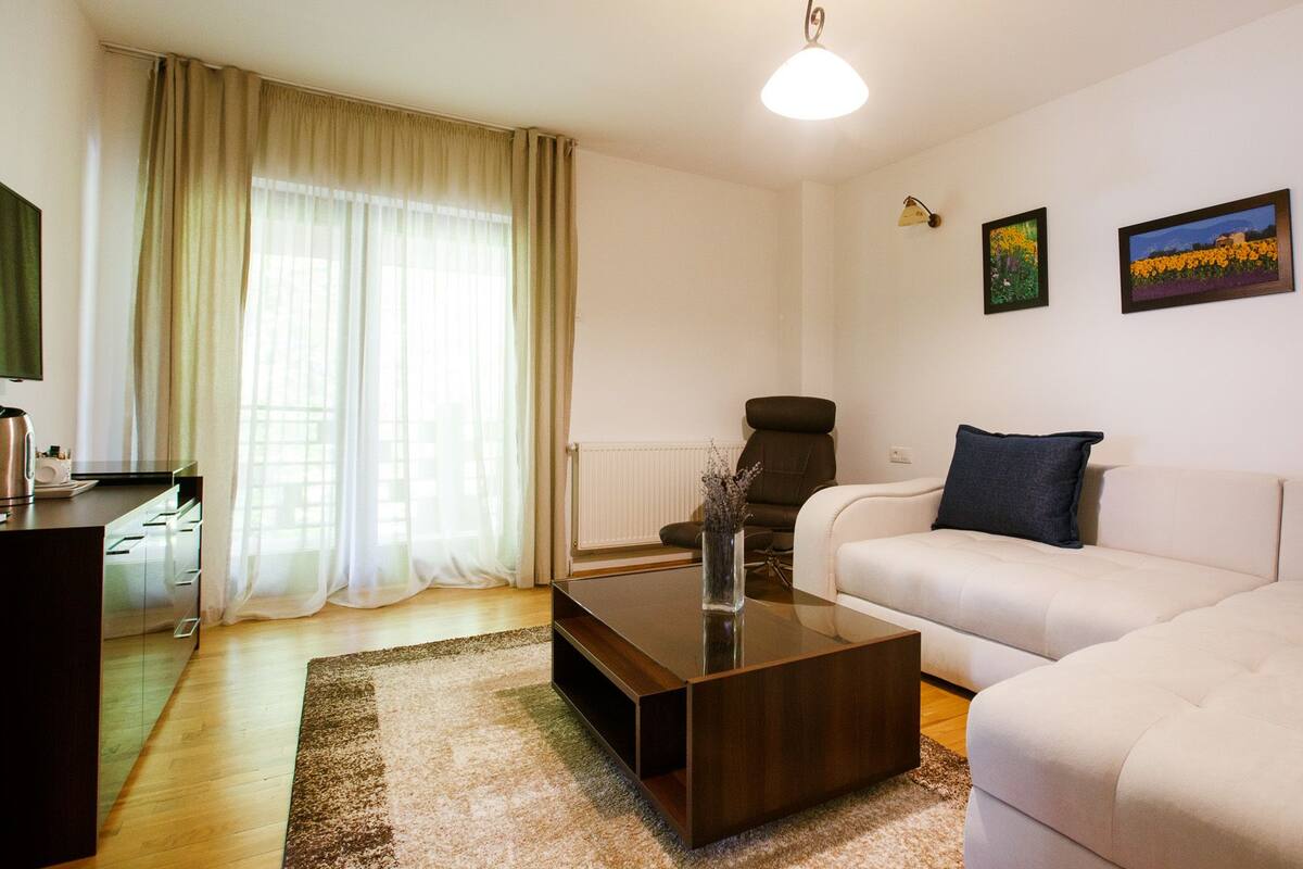 Un salon moderne comprenant un canapé, une table basse, un fauteuil et un coin repas avec une table et des chaises. Deux tableaux sont accrochés au mur.