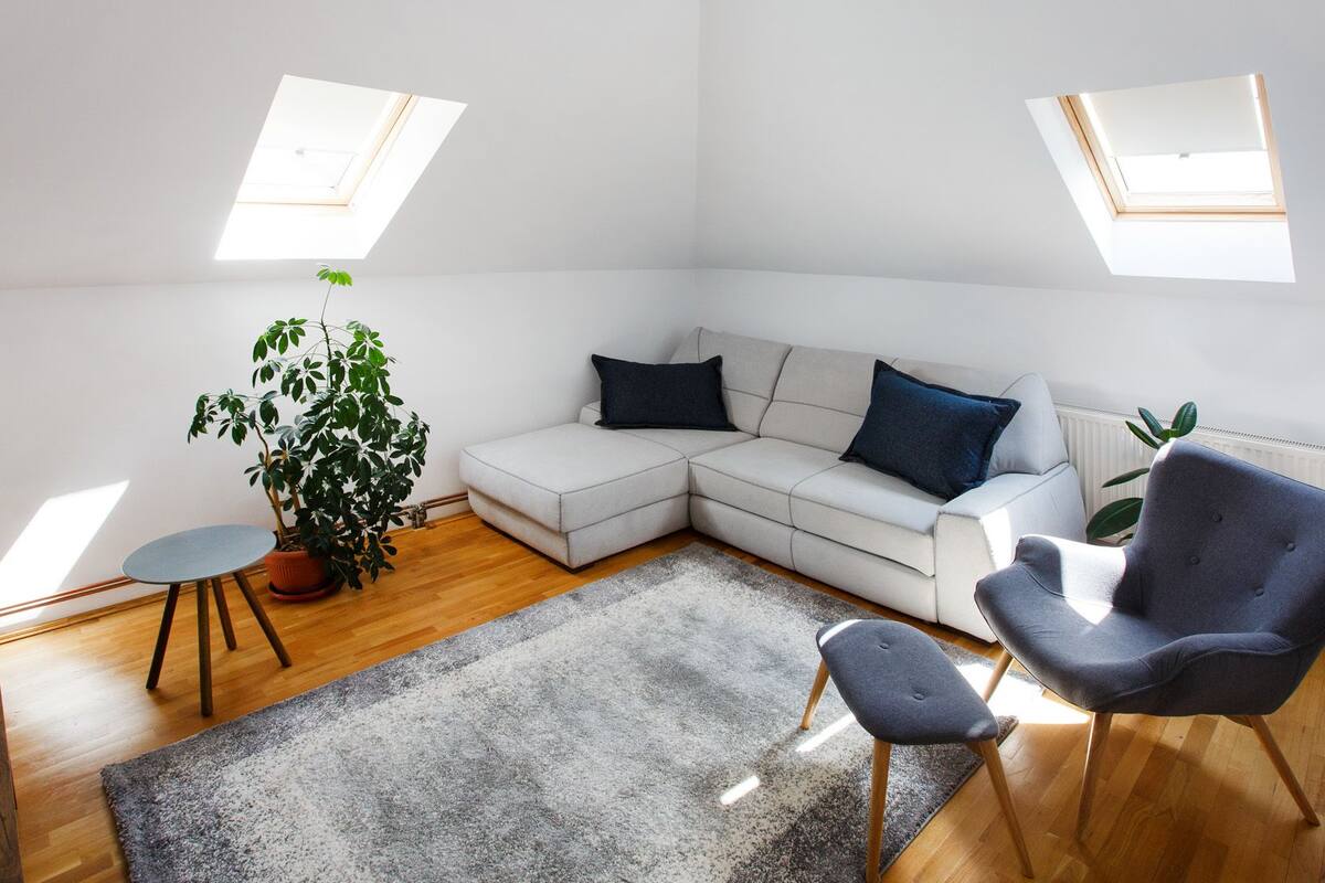 Un salon moderne avec un canapé d’angle, un fauteuil gris, une petite table ronde et une plante en pot.