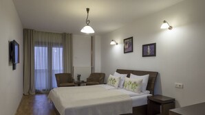 Un dormitorio con una cama, dos sillas, un televisor y un ventanal con cortinas.