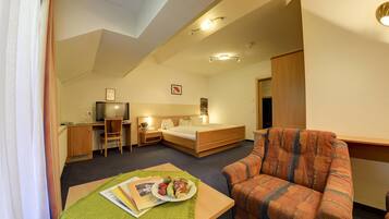 A hotel room with a bed, a desk, a chair, a television, and a dining table with a plate of fruit.