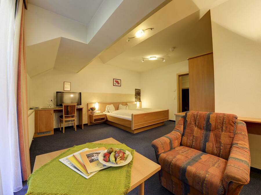 A hotel room with a bed, a desk, a chair, a television, and a dining table with a plate of fruit.