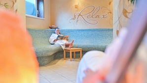 A person reading on a blue sofa in a room with a 'Relax' wall decoration. - Flattacher Hof (Flattach)