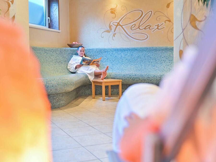 A person reading on a blue sofa in a room with a 'Relax' wall decoration.