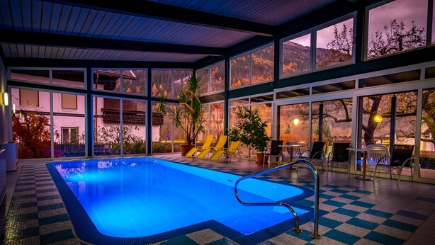 An indoor swimming pool with checkered flooring, large windows, and a view of a mountain landscape. - Flattacher Hof (Flattach)