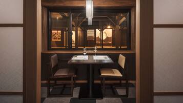 A dining area with a table set for two, two chairs, and a hanging light fixture.