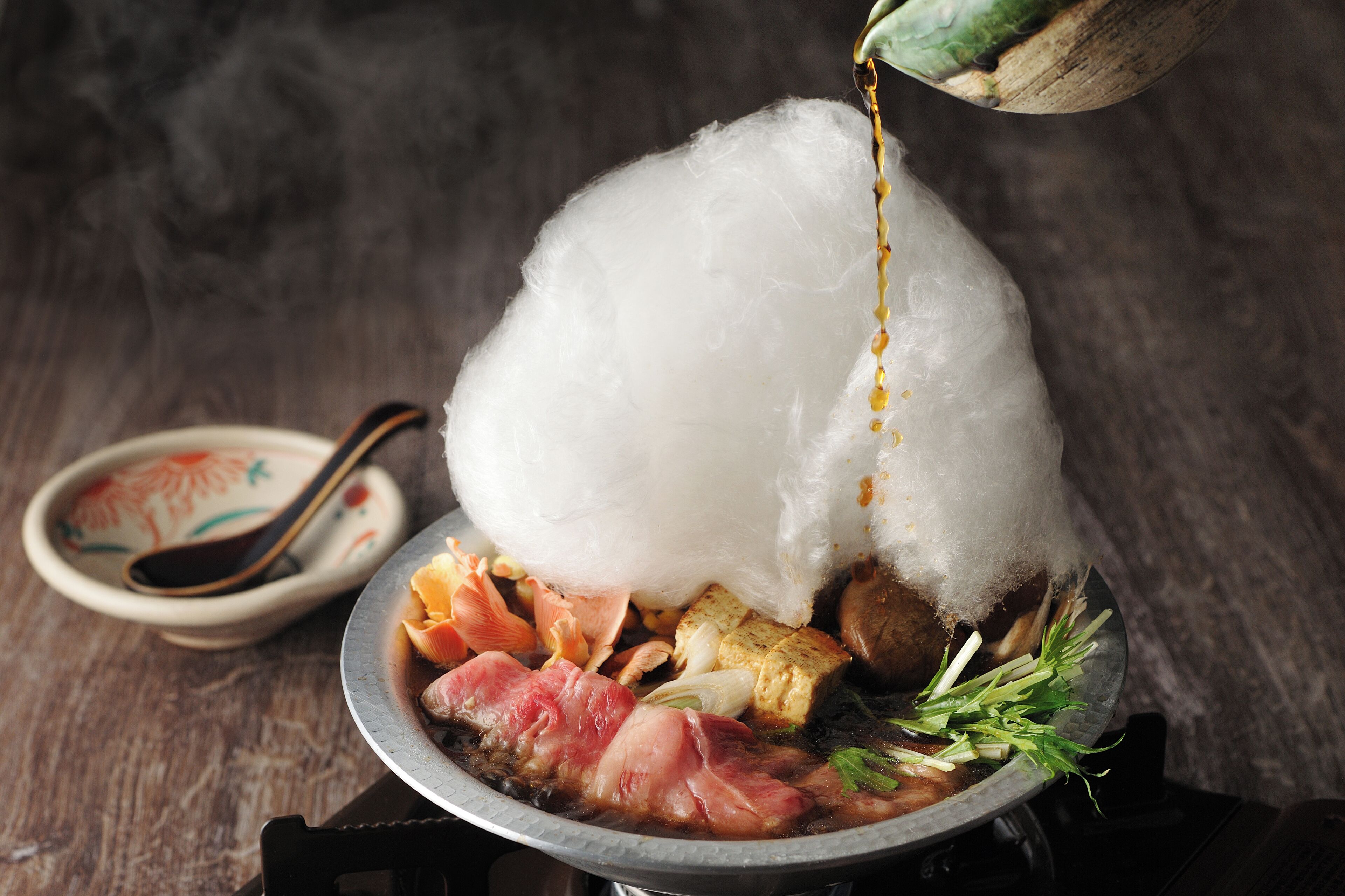 A hot pot meal with various ingredients and a large piece of white food being added.