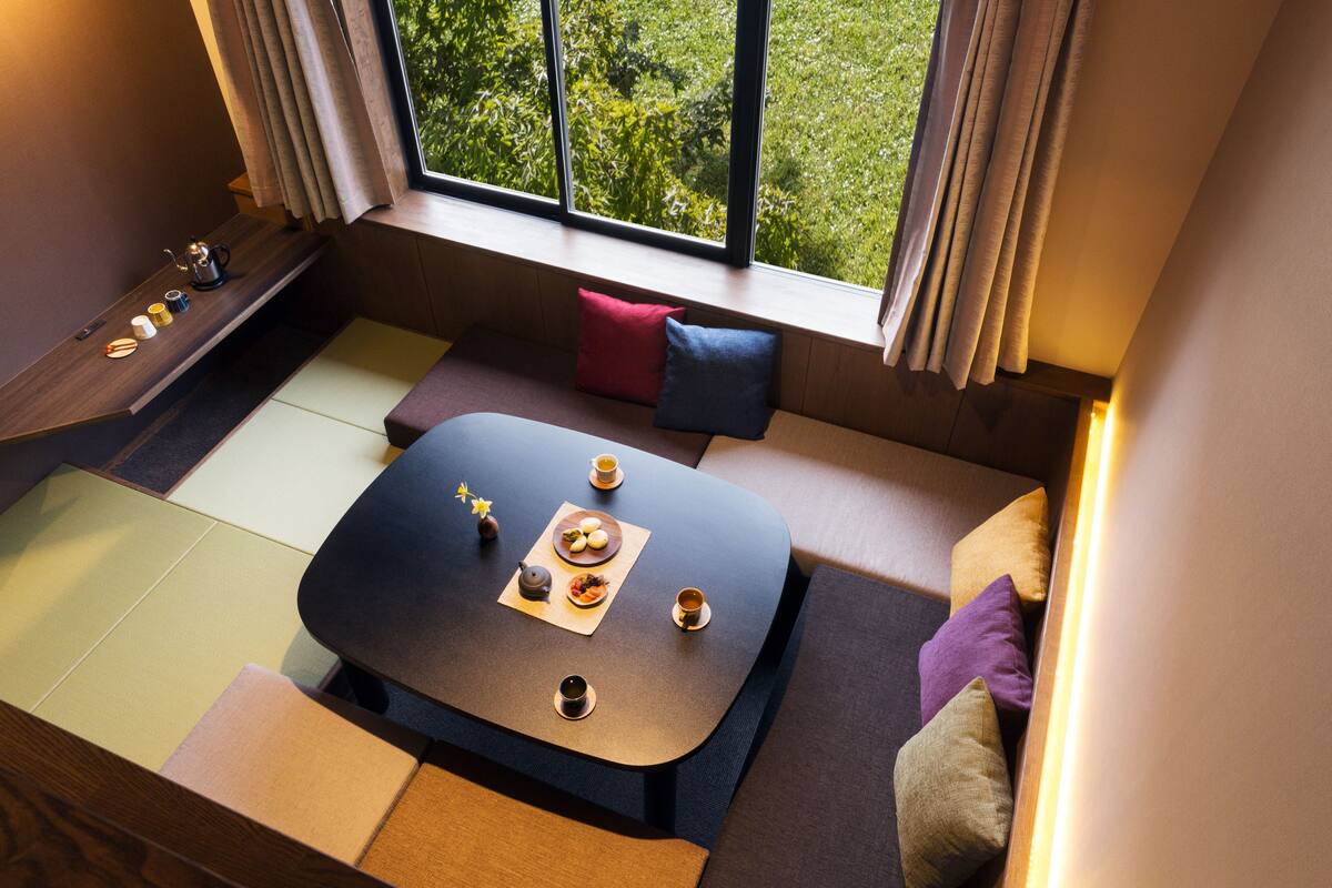 A cozy seating area with a low table set for tea, cushions, and a view of greenery outside.