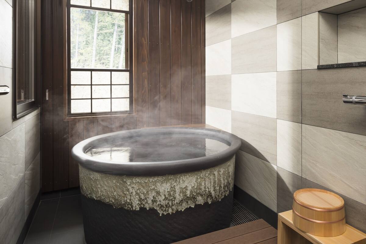 A steam bath with a wooden exterior, a window with a view of trees, and a tiled wall.
