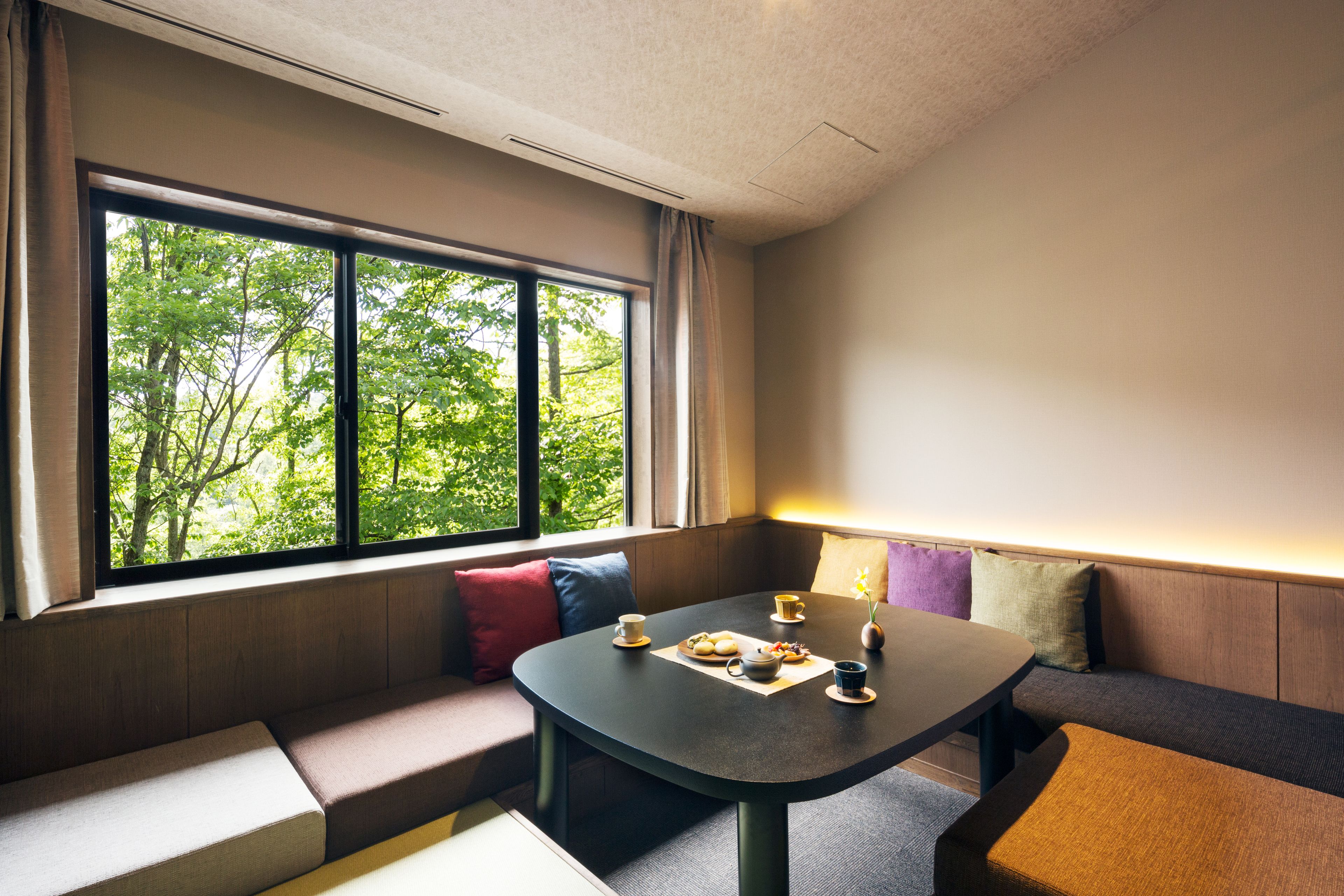 A room with a large window, a round table, and a bench along the wall.