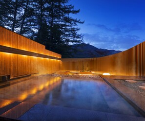 A modern spa with a wooden wall and a reflective pool, surrounded by trees and mountains. - Hoshino Resorts KAI Alps (Omachi)