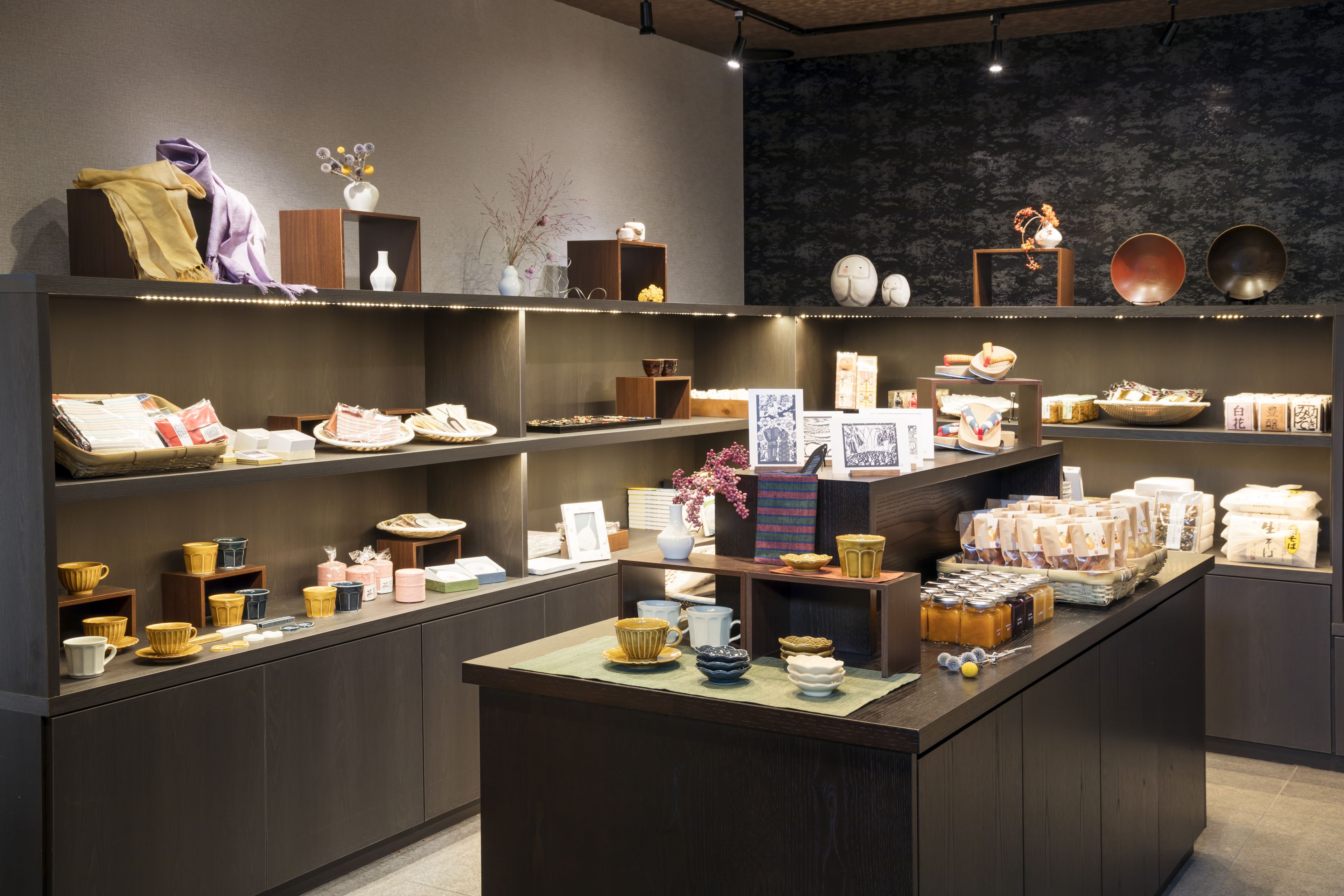 A modern retail space with shelves displaying various ceramic items, a central counter with packaged goods, and decorative elements like vases and bowls.