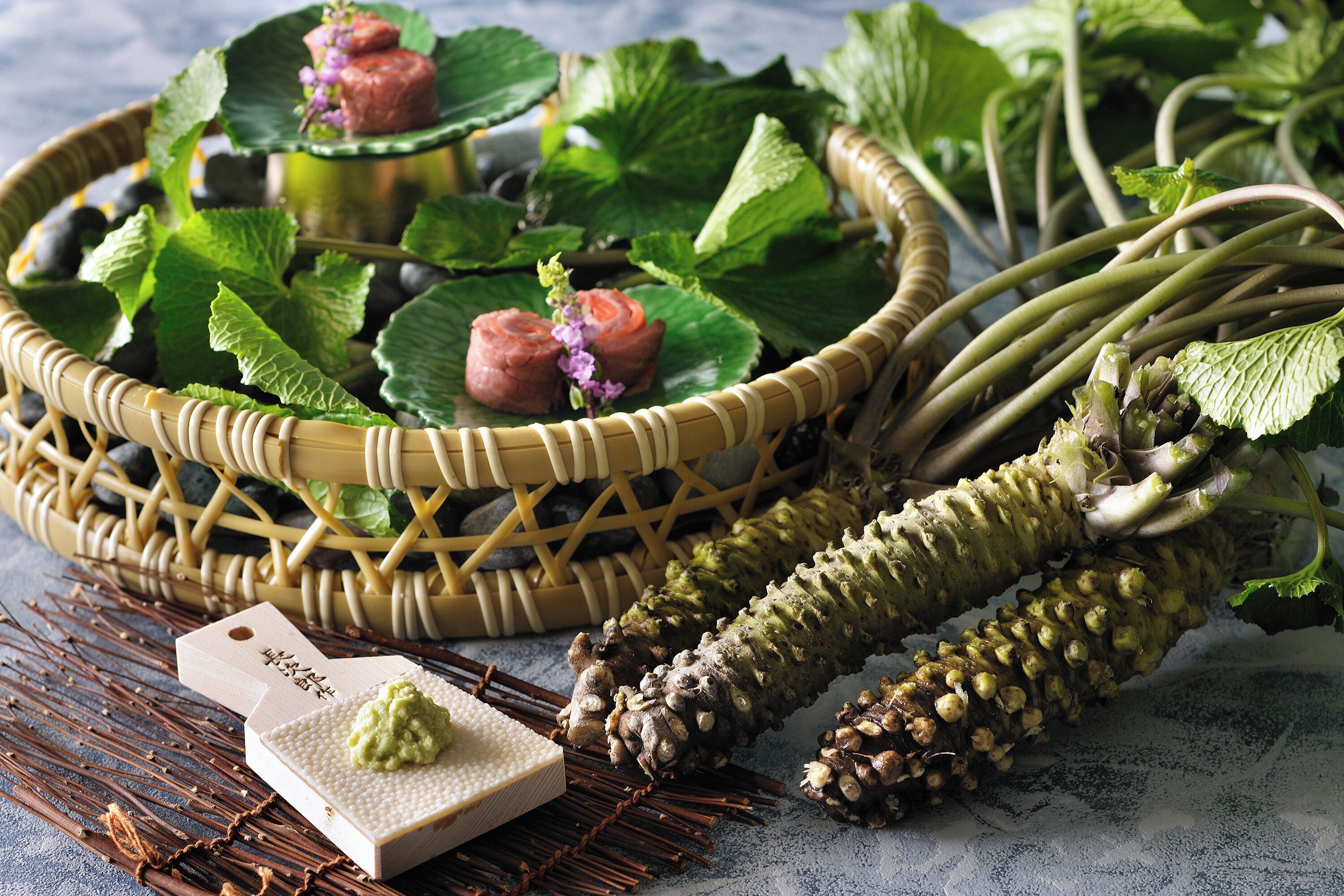 A wicker basket with a wooden cutting board and a tag, surrounded by fresh herbs and a large root vegetable.