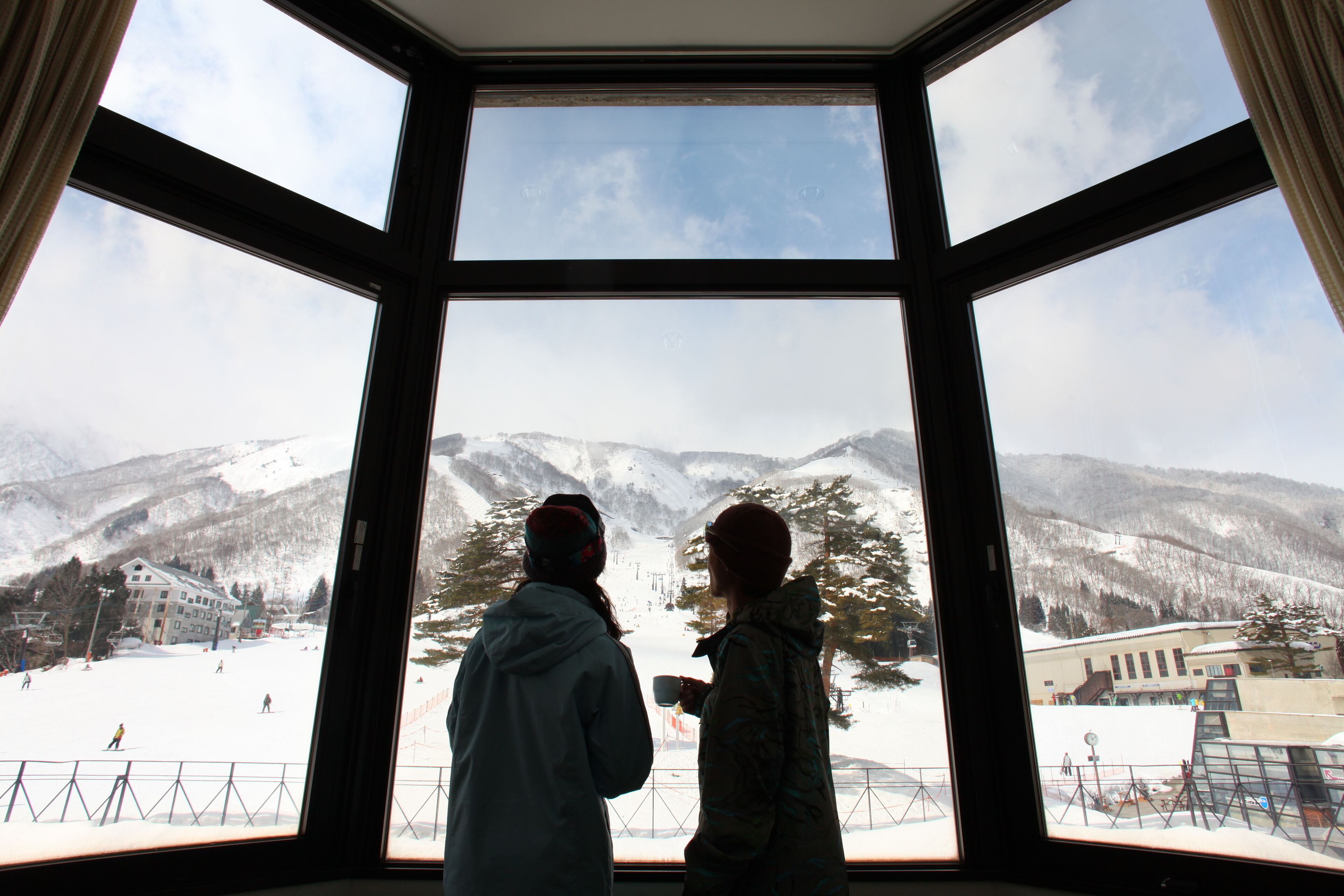 Two people standing by a large window overlooking a snowy mountain landscape.