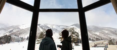 Two people standing by a large window overlooking a snowy mountain landscape.