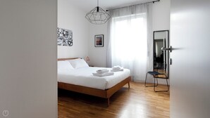 A bedroom with a wooden bed, white linens, a geometric pendant light, a framed picture, and a mirror on the wall. - Italianway   - Scarlatti (Milan)