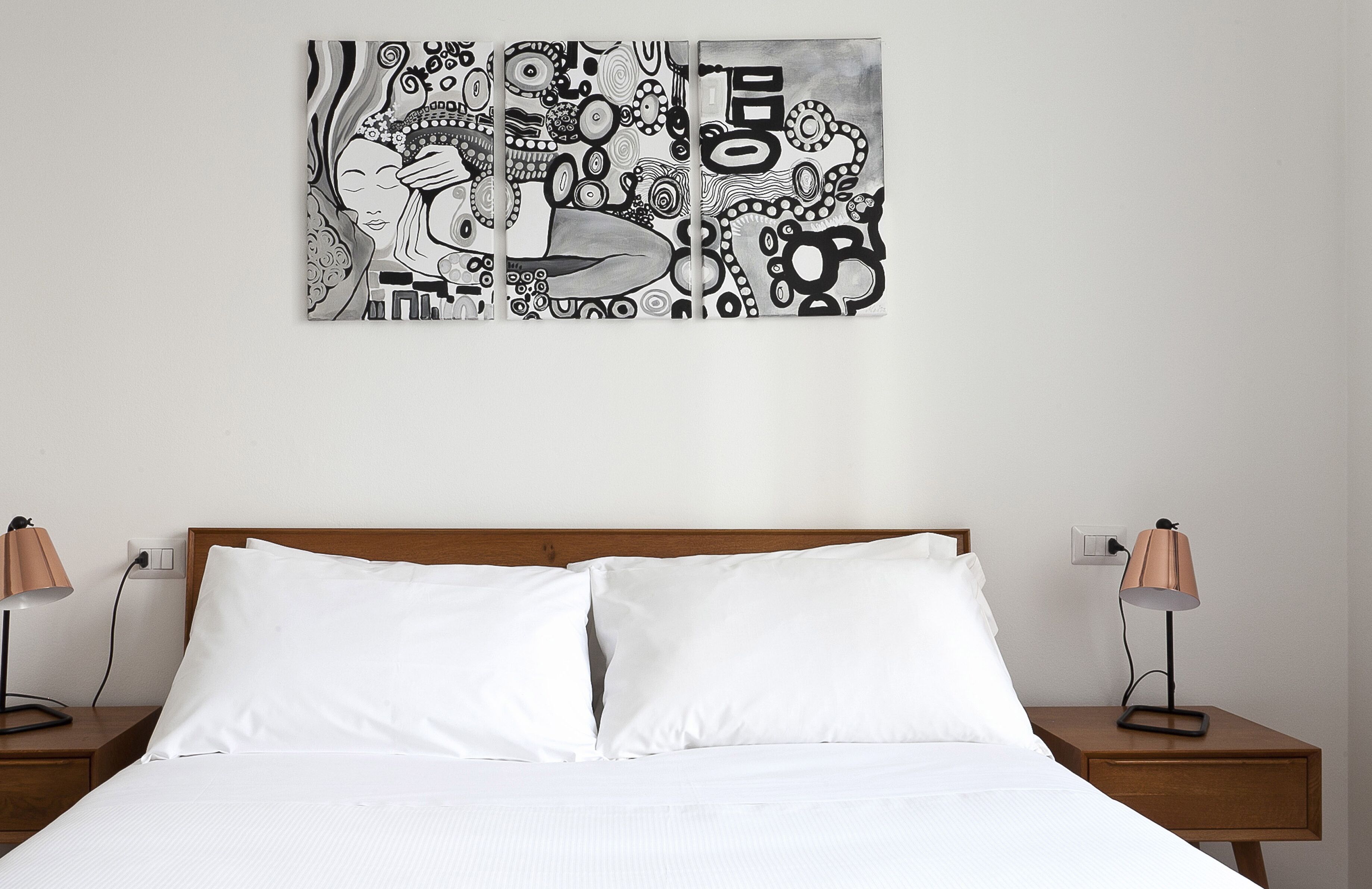 A bedroom with a wooden headboard, two bedside tables with lamps, and a large abstract artwork on the wall.