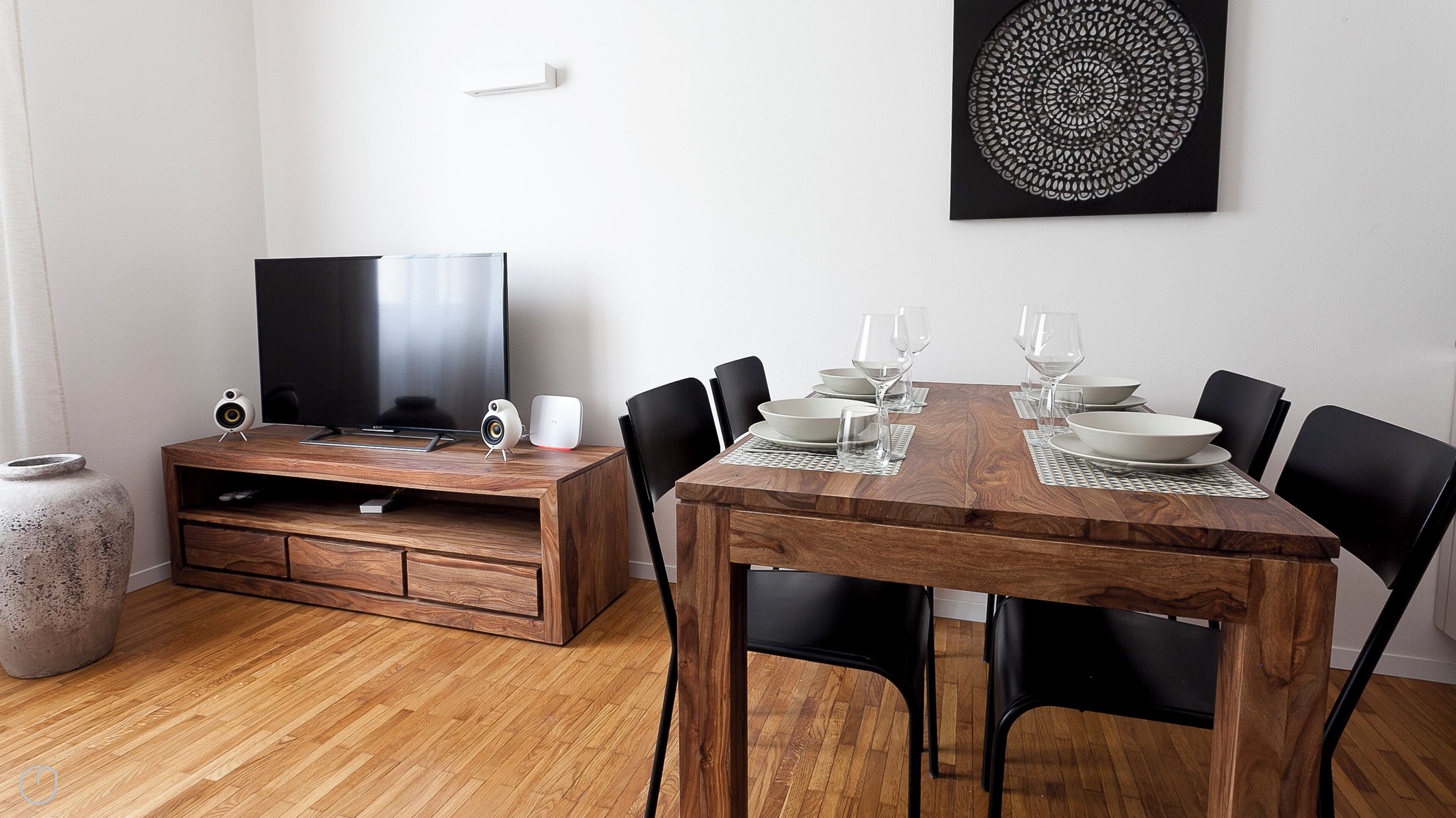 A dining area with a wooden table set for four, black chairs, and a television on a wooden stand.