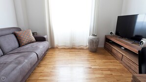 A modern living room with a grey sofa, a patterned throw pillow, a large vase, a wooden TV stand, and a flat-screen TV. - Italianway   - Scarlatti (Milan)