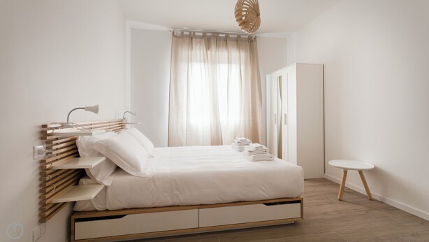 Ein schlicht eingerichtetes Schlafzimmer mit Bett, Nachttischen, einem Kleiderschrank und einem kleinen runden Tisch.