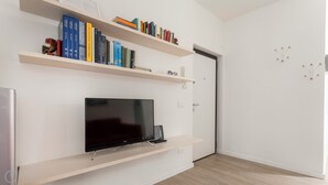 Ein modernes Wohnzimmer mit einem Flachbildfernseher auf einem Lowboard, Holzregalen mit Büchern und einer Tür mit Kleiderhaken.