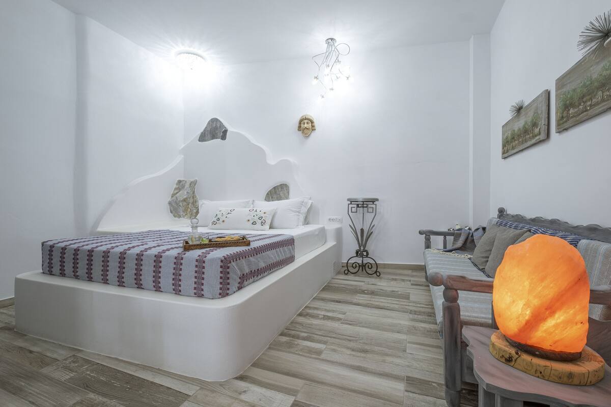 Ein modernes Schlafzimmer mit einem weißen Bett, Holzboden, einer Couch und einer Wanddekoration.