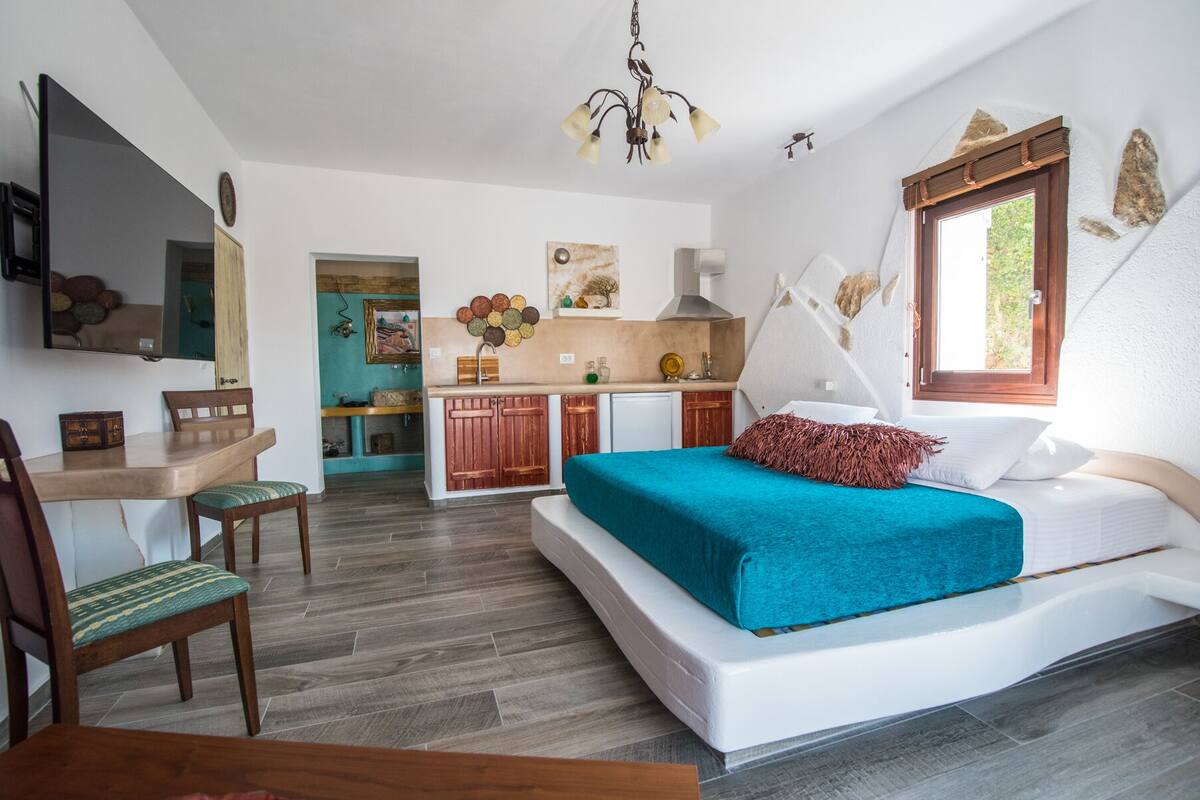 Ein kleines Hotelzimmer mit Bett, Schreibtisch und einer Küchenzeile.