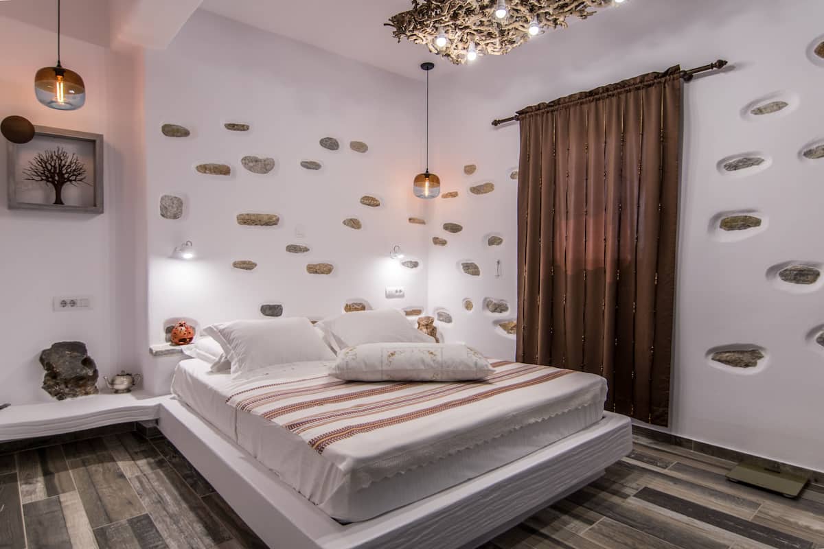 Ein modernes Schlafzimmer mit einem großen Bett, einer Wand mit eingelassenen Steinen, einer Kronleuchter und einem gerahmten Bild.