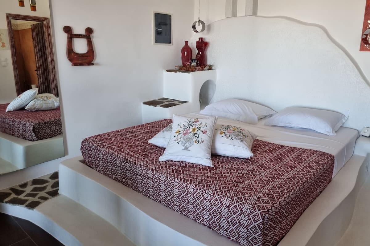 Ein Schlafzimmer mit einem gemusterten Bettüberwurf, einem Spiegel, einem Wanddekor und einem kleinen Nachttisch.