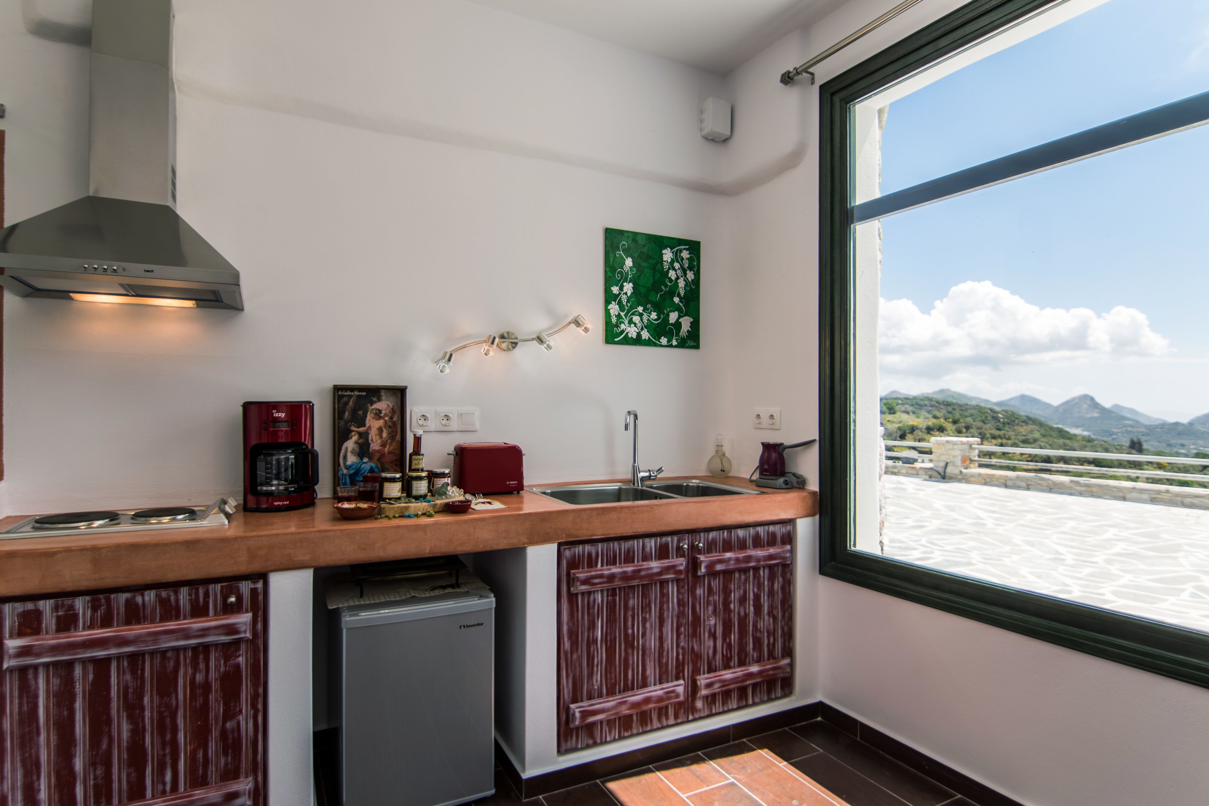 A kitchen with a view of mountains through a large window, a coffee maker, a toaster, and a sink.