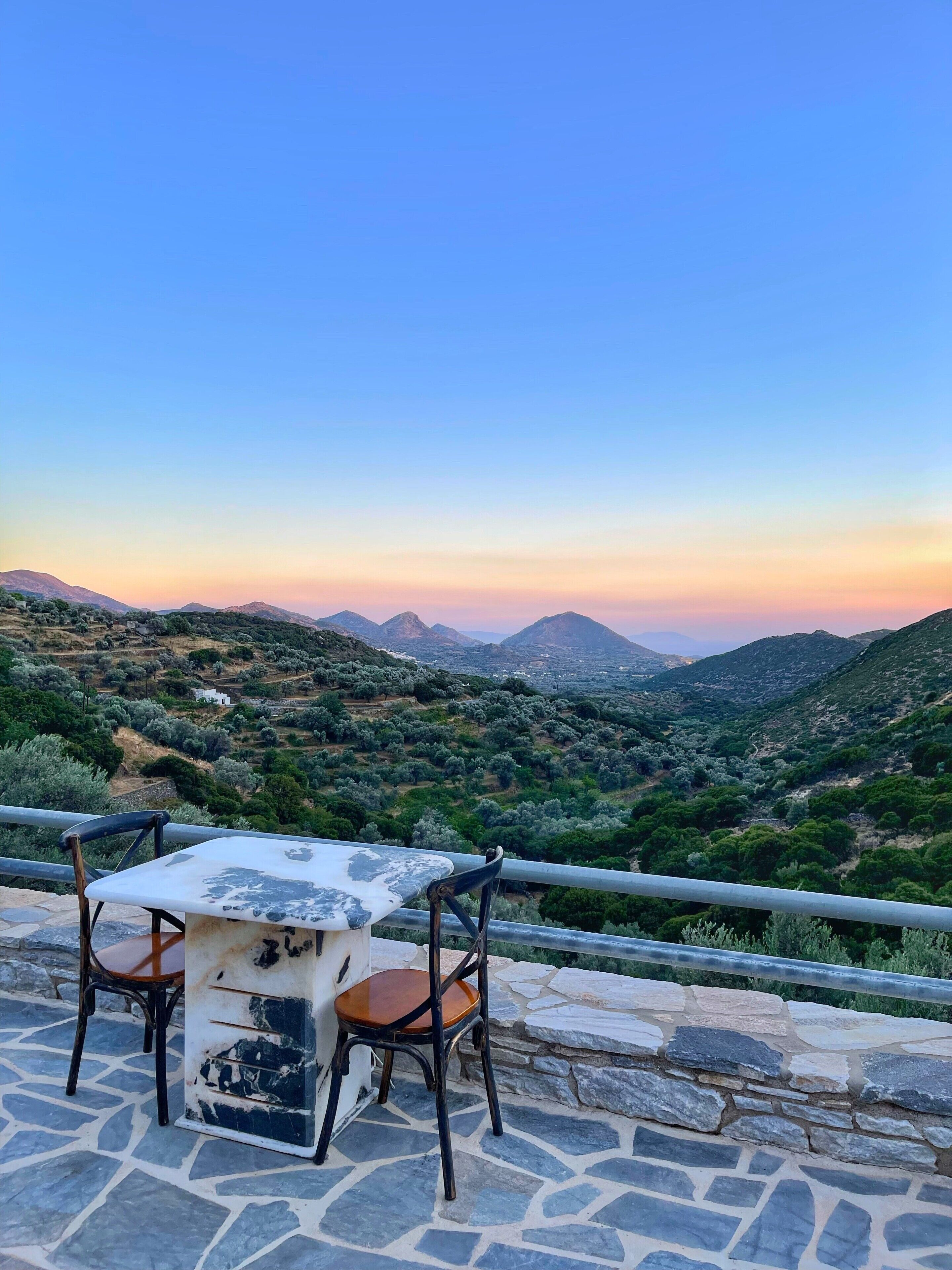 Una mesa de piedra con dos sillas en una terraza con vistas a un paisaje montañoso.