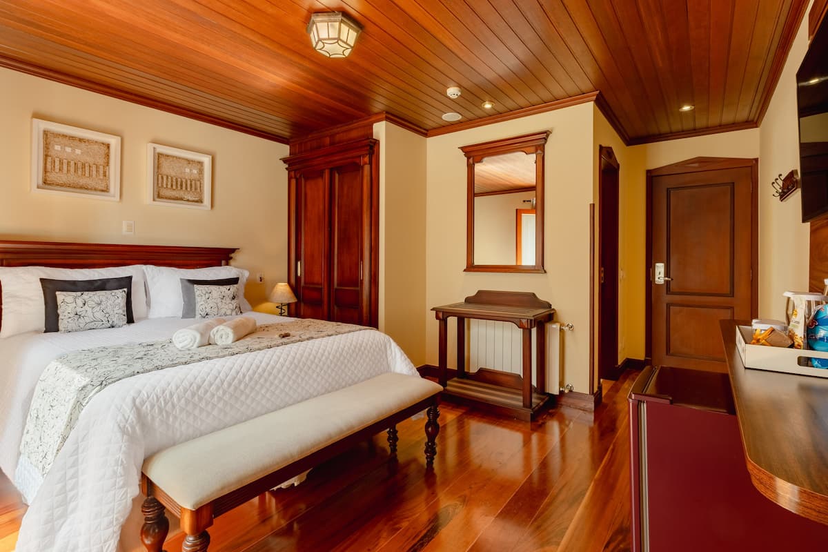 A bedroom with a large bed, wooden headboard, a bench, a nightstand, and a dresser.