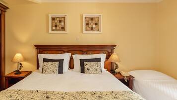 A hotel room with a large bed, two bedside tables, a wooden headboard, two framed artworks on the wall, and a bedside lamp.