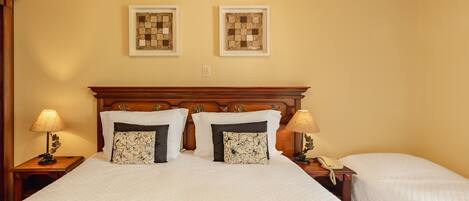 A hotel room with a large bed, two bedside tables, a wooden headboard, two framed artworks on the wall, and a bedside lamp.