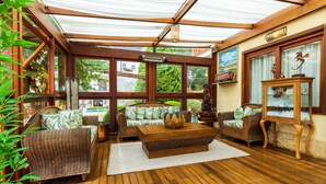 Un solárium con suelo de madera, mobiliario de mimbre y ventanas amplias.