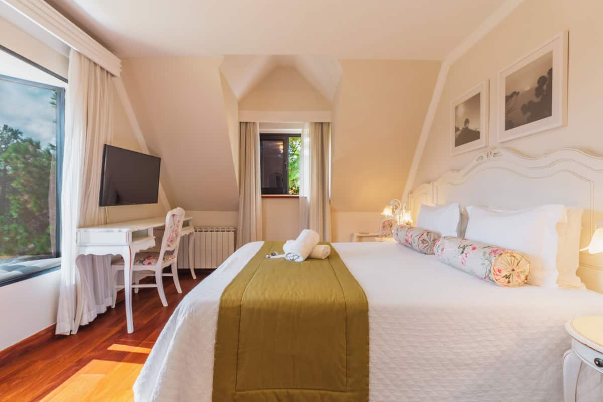 Een hotelkamer met een groot bed, een bureau met stoel, een televisie en een raam met gordijnen.