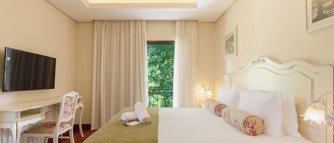 Una habitación de hotel con cama, escritorio, silla, televisor y ventana con cortinas.