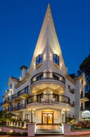 A multi-story hotel with a distinctive triangular roof, multiple balconies, and a well-lit entrance. - Pousada D'Biagy Premium (Campos do Jordão)