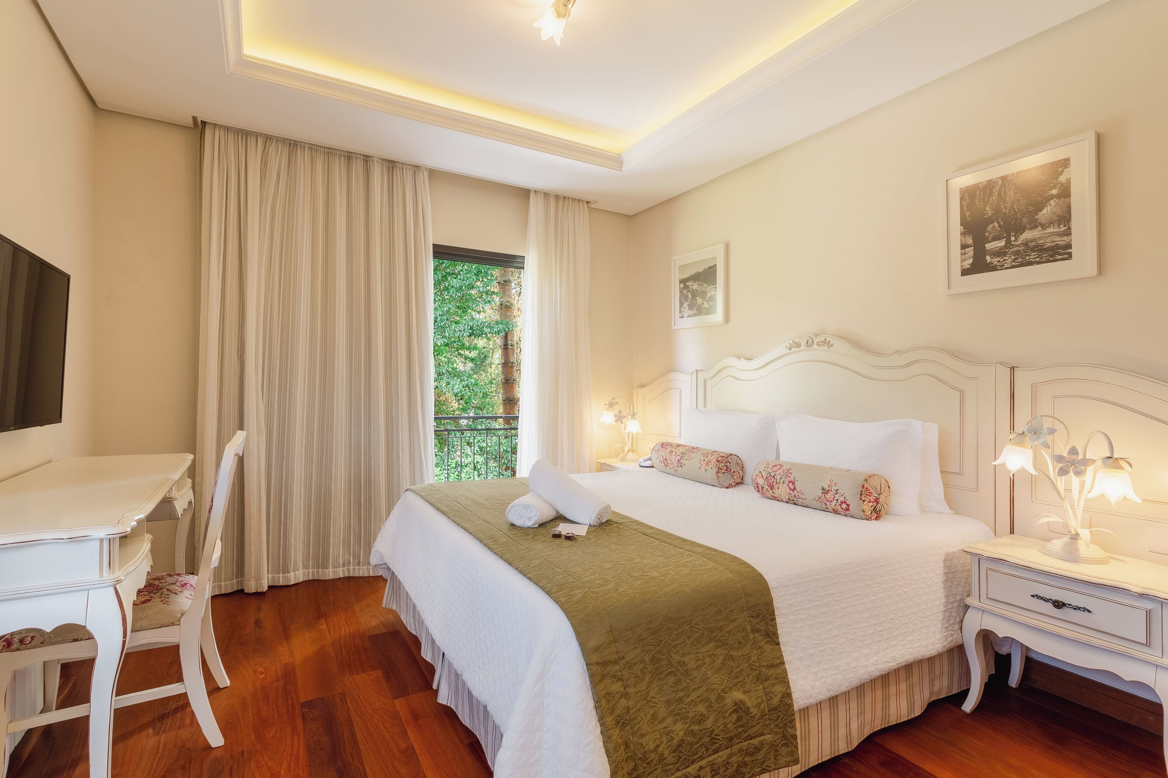 Une chambre d’hôtel comprenant un lit, un bureau, une chaise, une table de chevet et une fenêtre avec des rideaux.