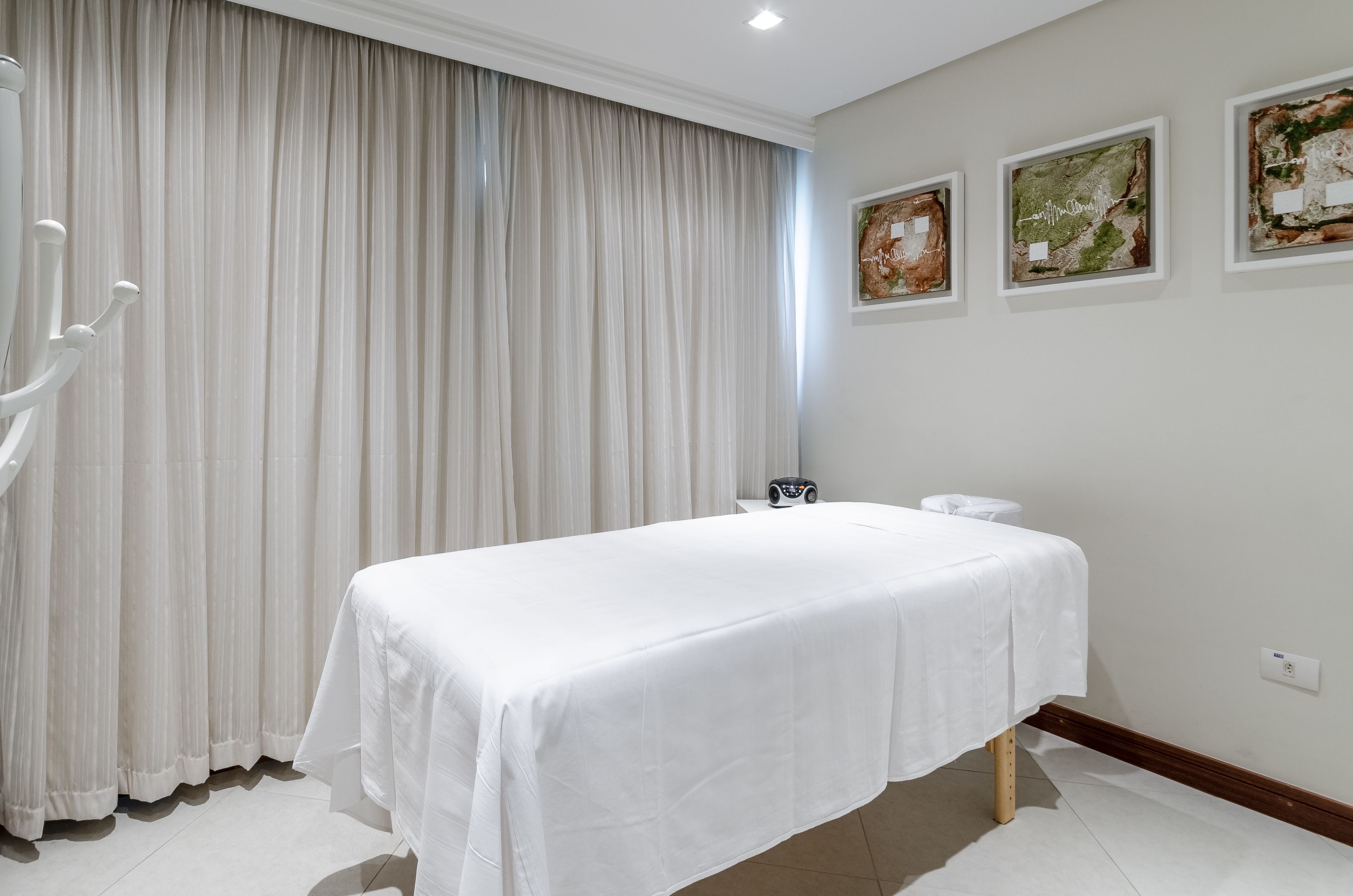Quarto limpo e moderno com uma cama, cortina branca e três obras de arte emolduradas na parede.