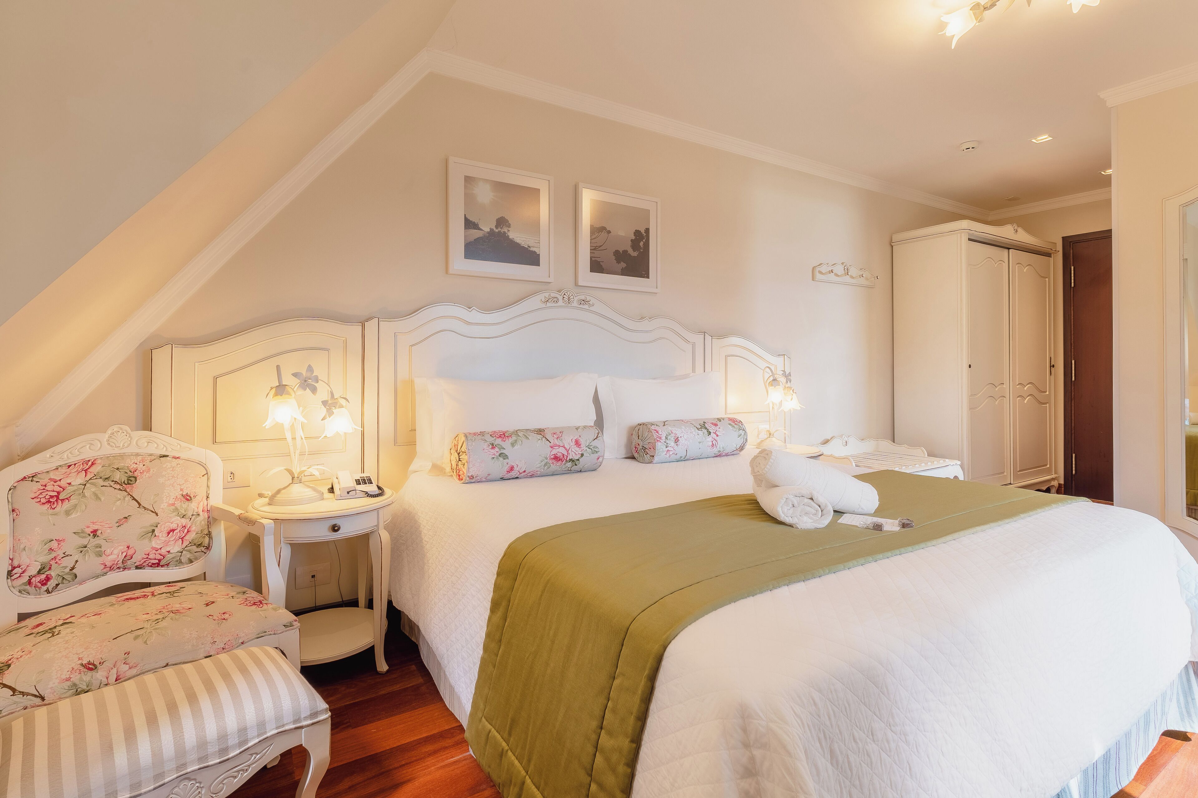 A bedroom with a large bed, a nightstand with a lamp, a chair, and a wardrobe.