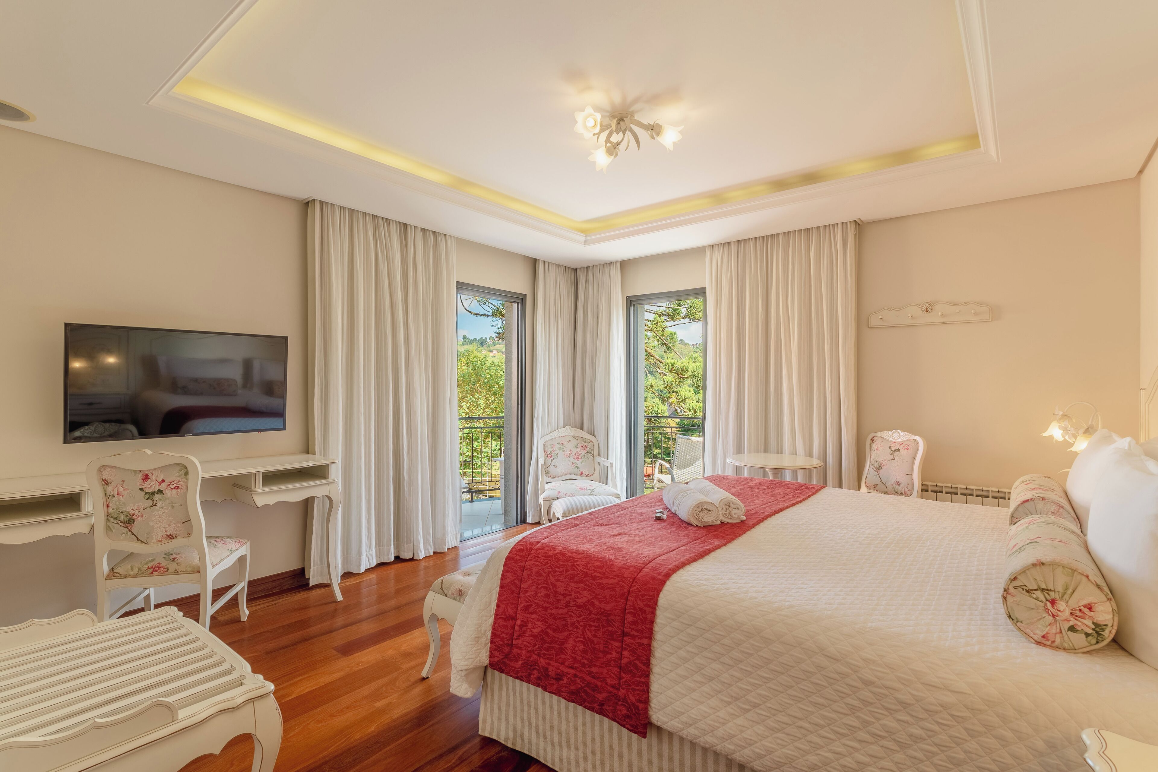 A bedroom with a large bed, a desk, and a TV. There are two chairs and a small table.
