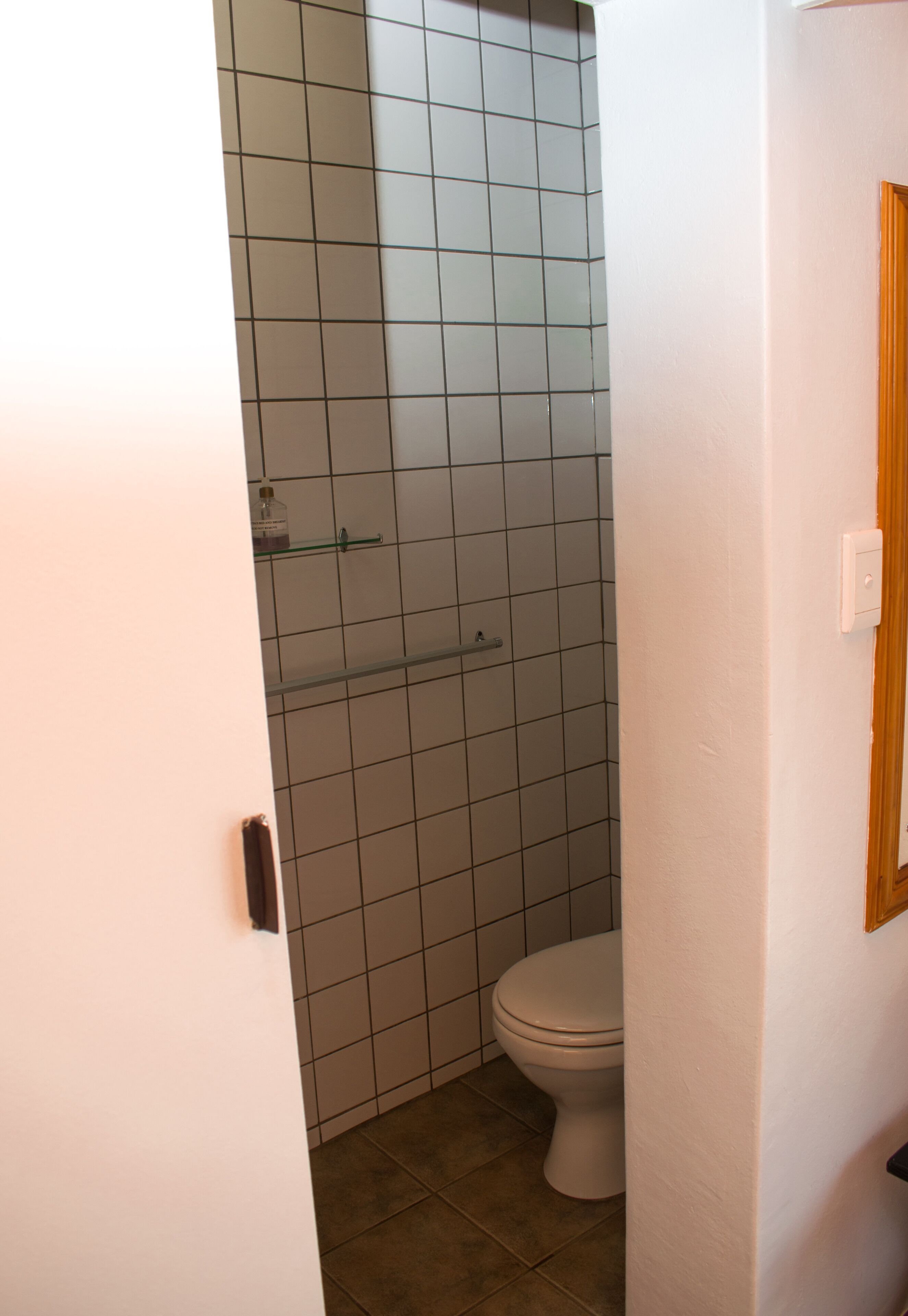 A bathroom with a toilet, a glass shower enclosure, and a white tiled wall.