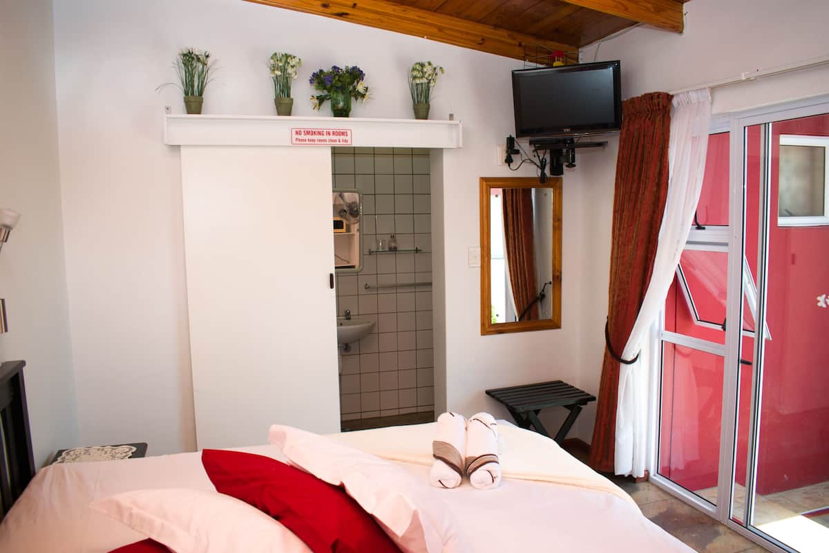 Quarto de hotel com cama, televisão, área de chuveiro e parede vermelha.