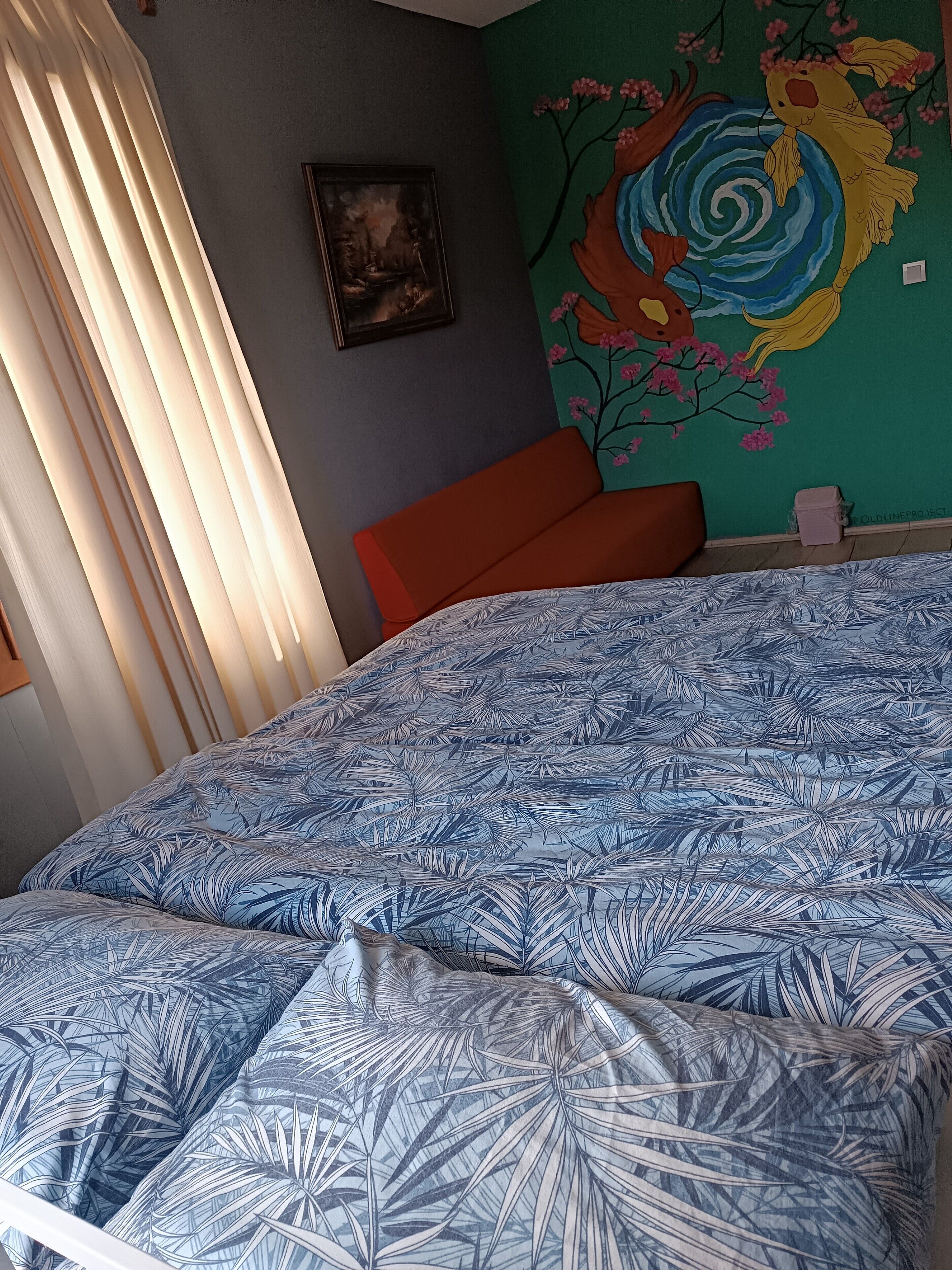 A bedroom with a bed, a painting, and a mural on the wall.