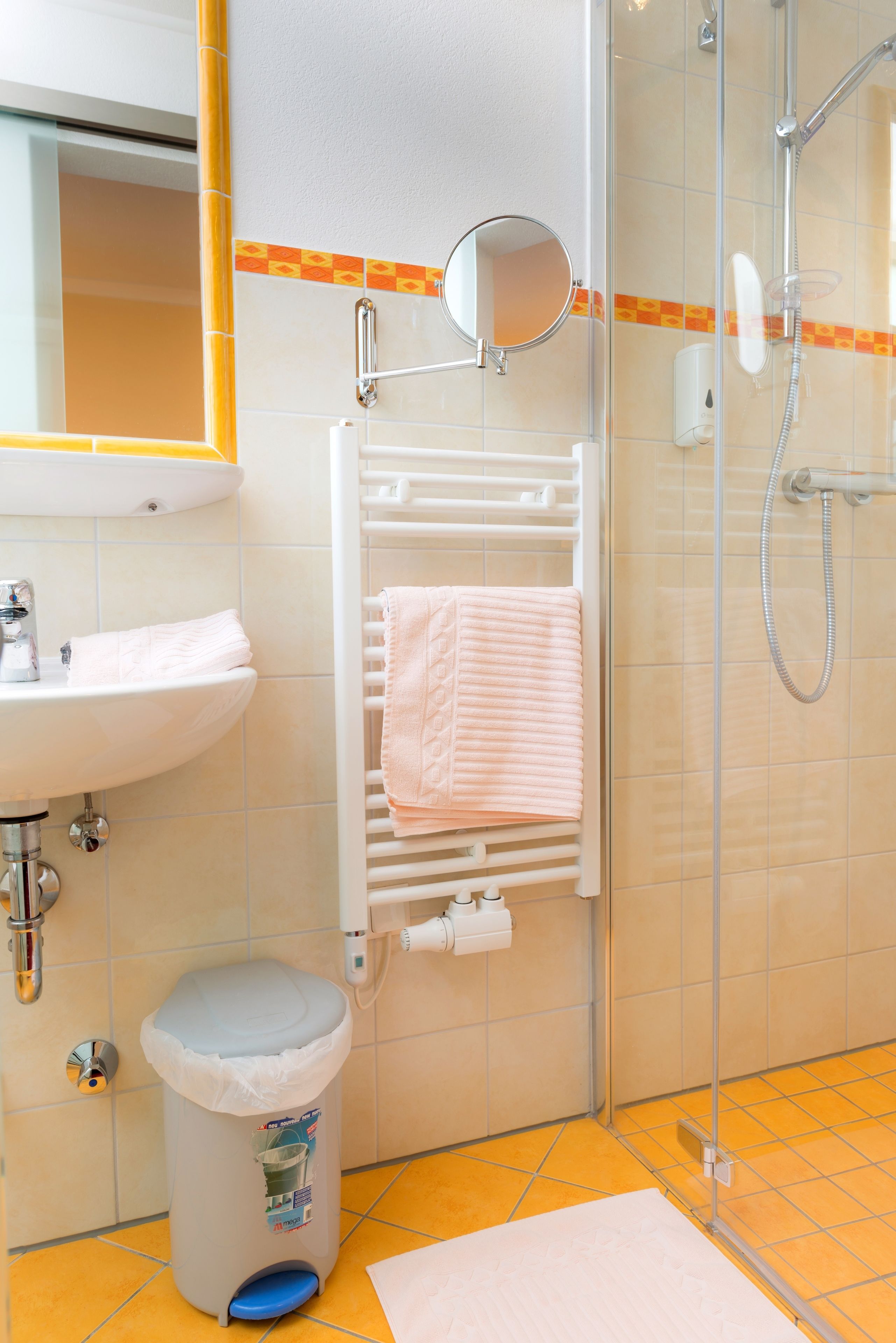 Een badkamer met een wastafel, spiegel, handdoekhouder, douche en een prullenbak.