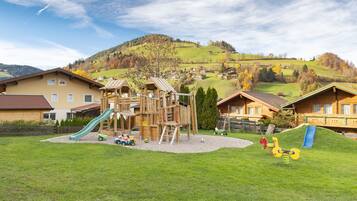 Un parque infantil con toboganes y estructuras para escalar, rodeado de casas y un paisaje montañoso.