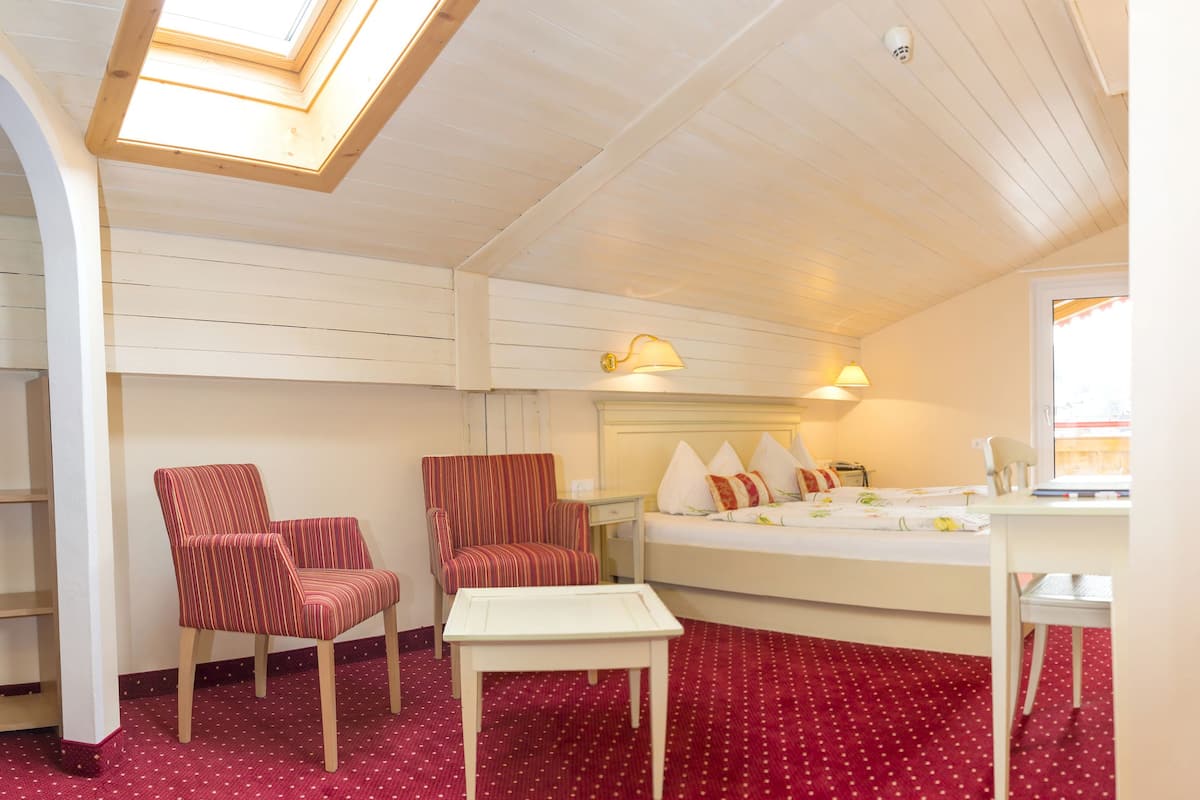 Une pièce comprenant un lit, deux chaises, une petite table et une fenêtre.