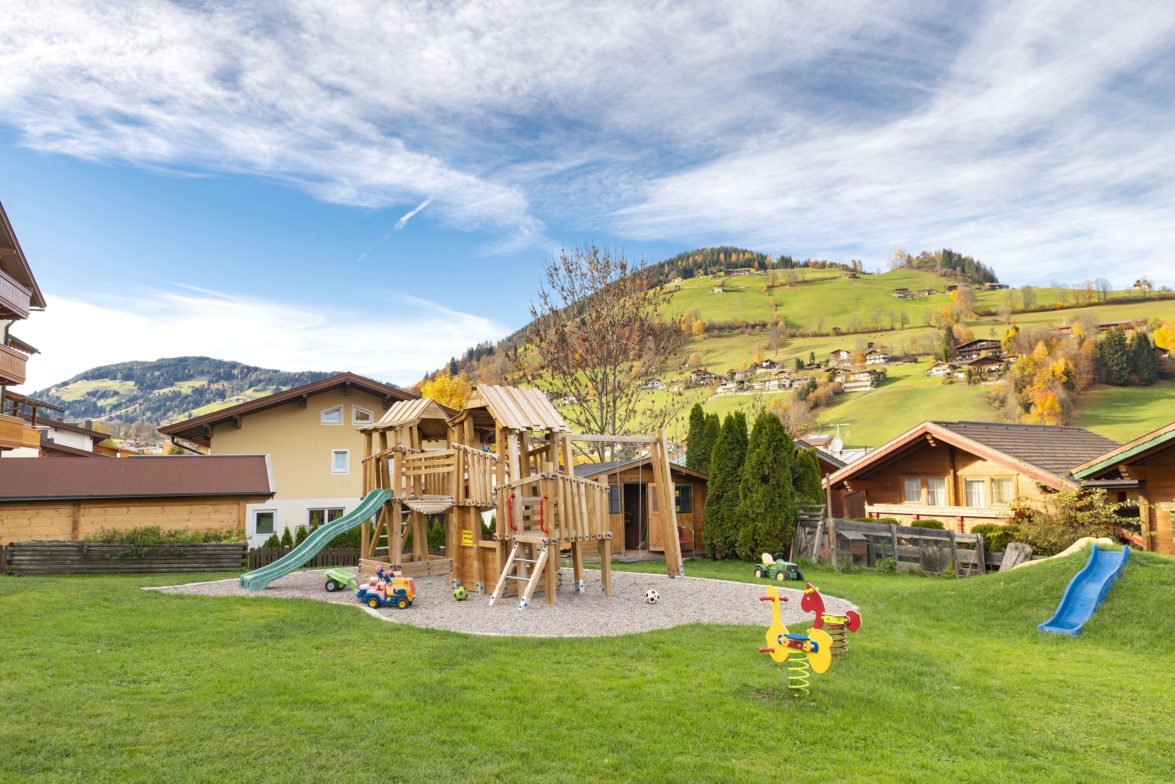 A playground with slides and climbing structures in a grassy area with houses in the background.