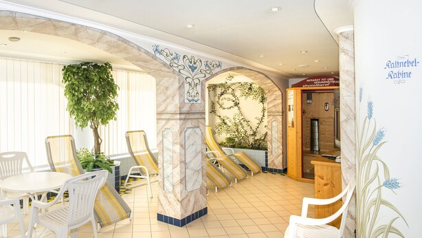 Vestíbulo de hotel con sillas y mesas blancas, un mostrador de recepción y una pared con un letrero.